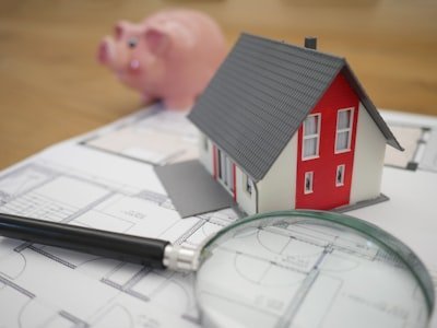 Model house on architectural plans with a magnifying glass and piggy bank, representing financial planning and credit management.