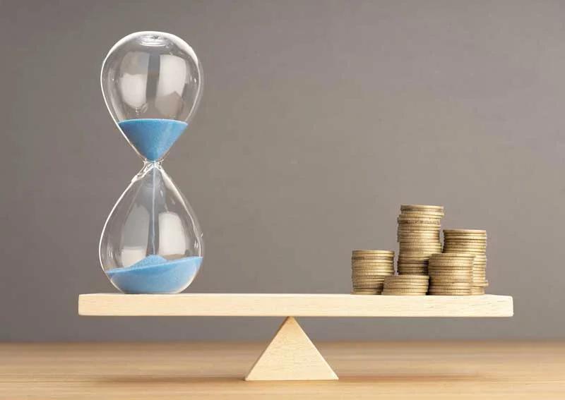Hourglass balancing on a scale with stacked coins, symbolizing the value of time in credit repair and financial management.